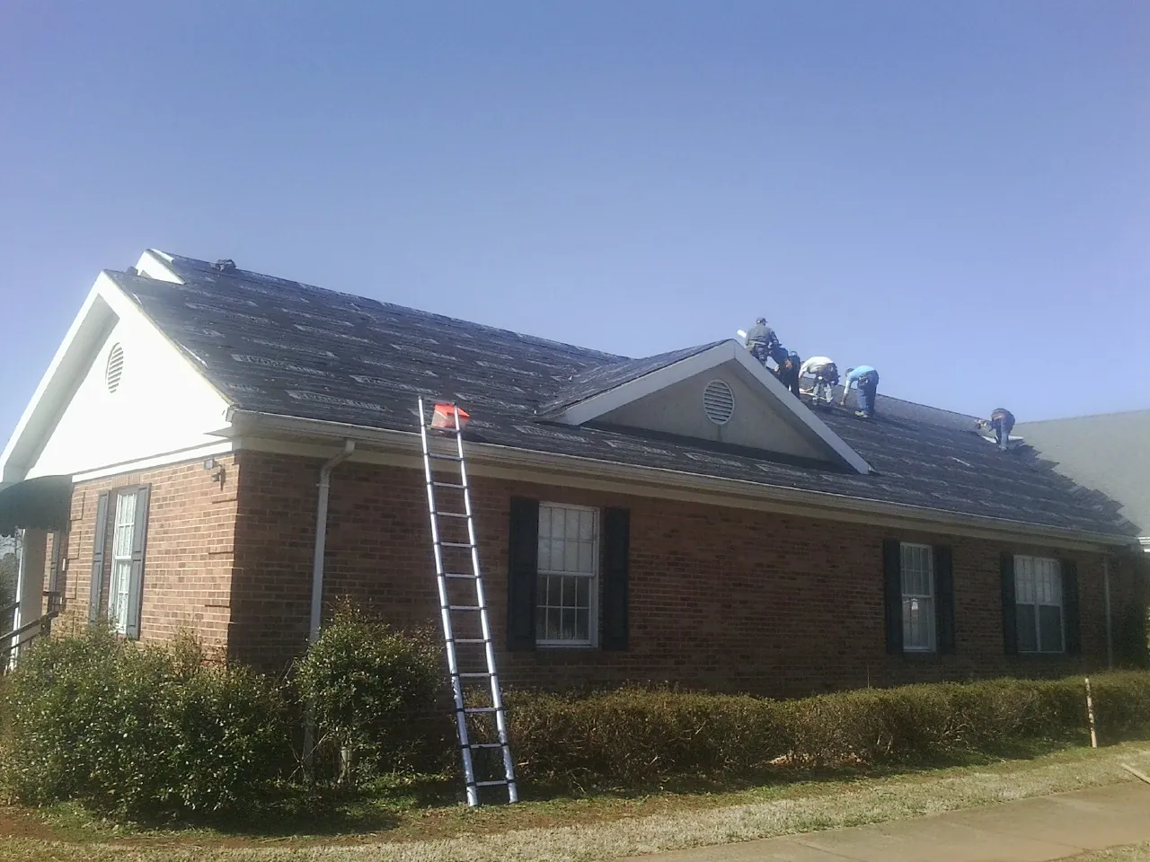 Crew tearing shingles off a brick ranch roof with a ladder set — Metal Roof Repair work by our crew in Palenville