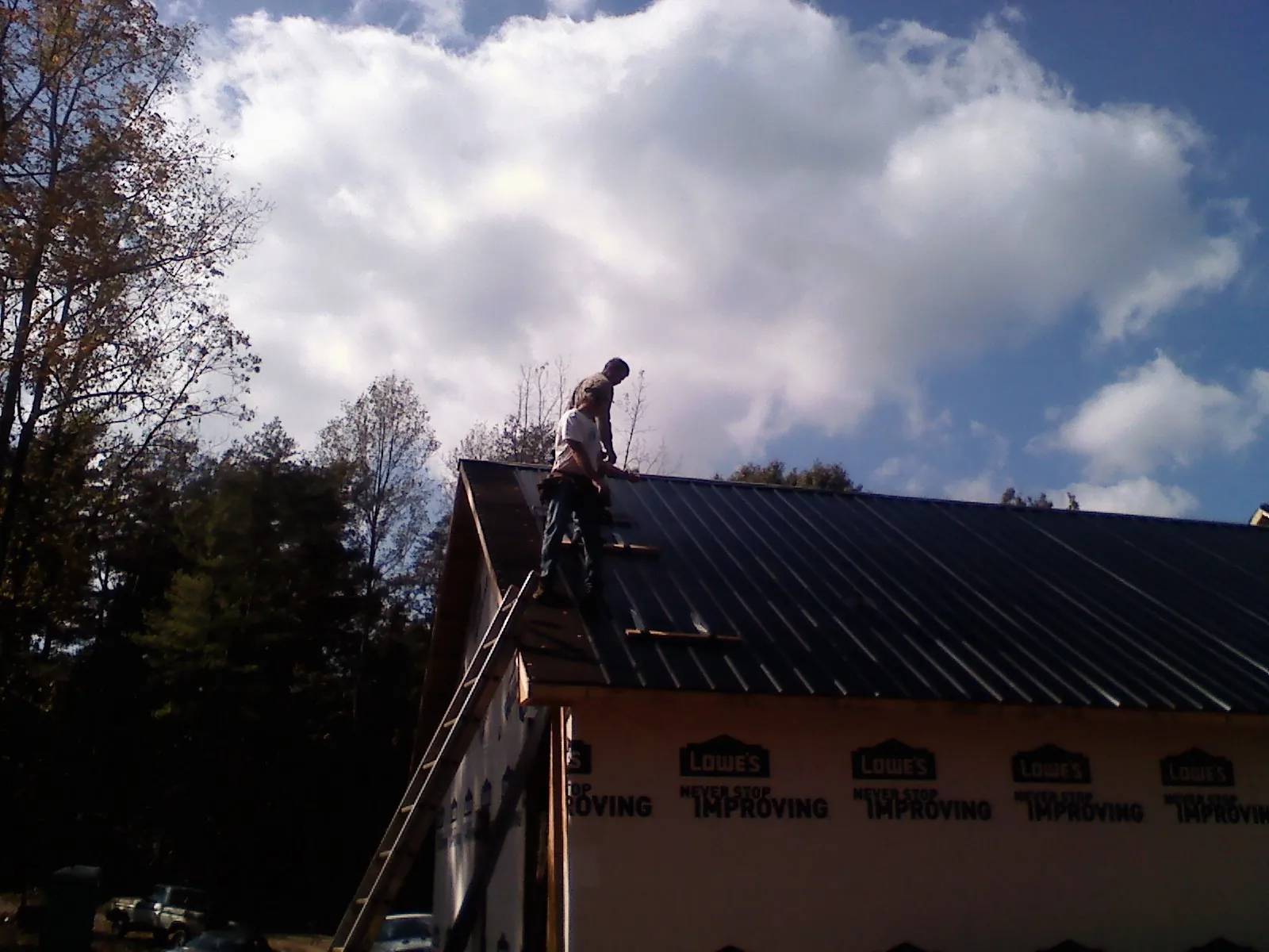 Roofer fastening dark metal panels high against a cloudy sky, from a Roof Inspection job in Palenville