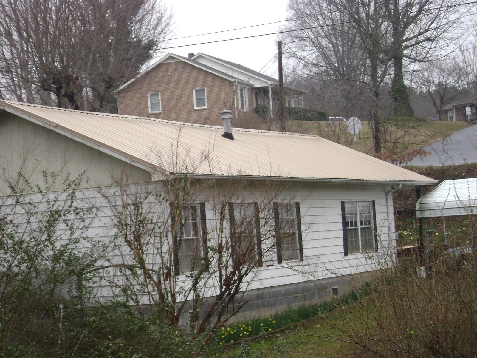 Tan metal roof on a white sided house set into a hillside — Commercial Roofing by Roofing Brothers in Palenville